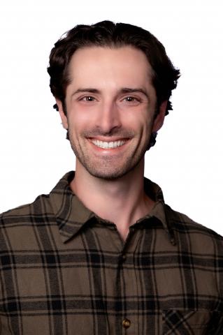 A professional headshot of a young adult white male with short brown hair wearing a green flannel