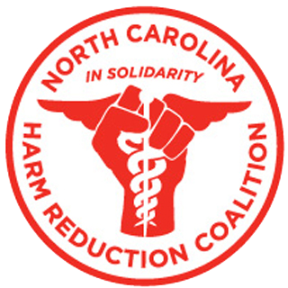 Circular logo for the North Carolina Harm Reduction Coalition. Red border with white background. Center features a medical caduceus symbol (staff with two intertwined serpents and wings) in red. Text curves along the top reading "NORTH CAROLINA" and along the bottom reading "HARM REDUCTION COALITION." Above the symbol it reads "In solidarity."