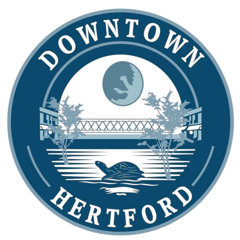 A dark blue circle with the words Downtown Hertford. In the center a turtle on a log sits in front of the water in the foreground. a bridge and the moon in the background.
